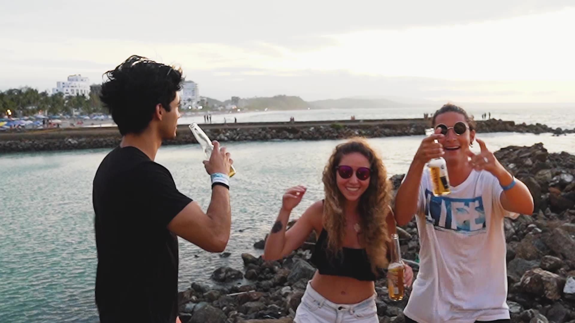 Friends with beers dancing on the rocks by the sea